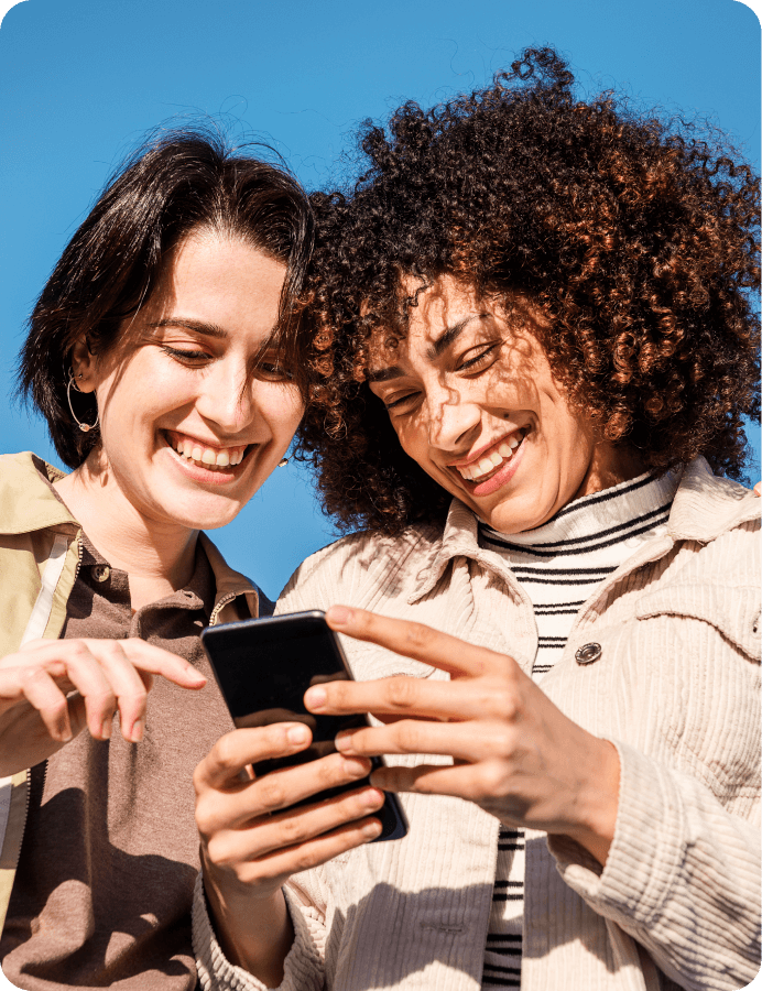 two women laughing when looking at a phone