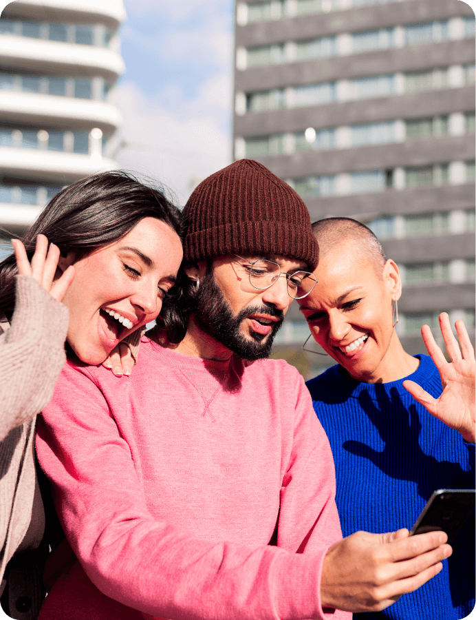 Three friends smiling and looking at a smartphone outdoors