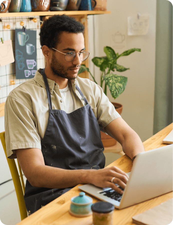 Man wearing an apron and glasses working on a laptop