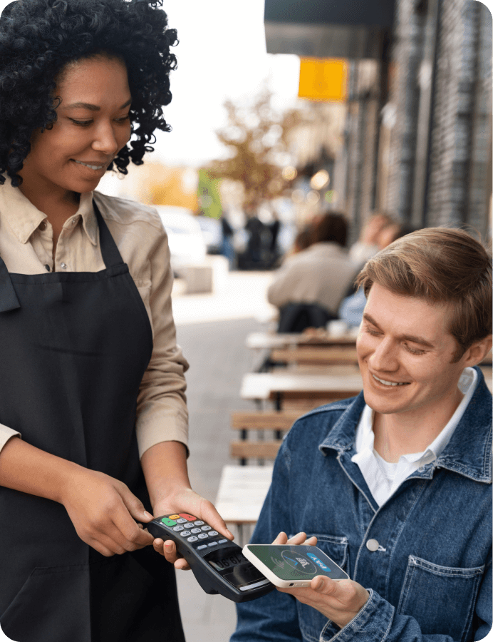 Smiling waiter holding a card reader while a customer makes a contactless payment